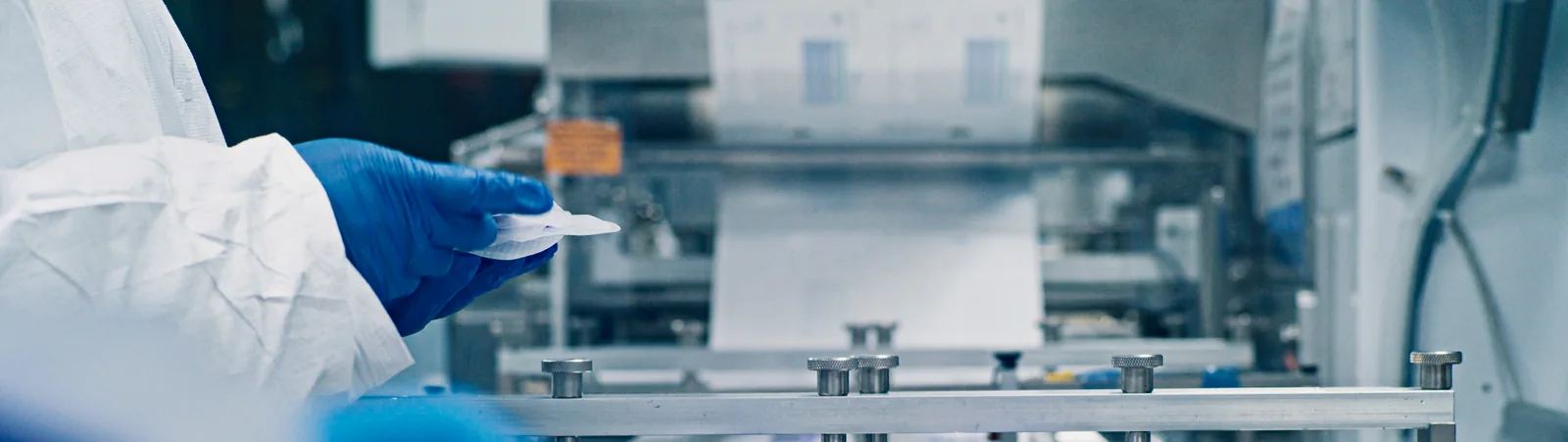 Gloved production operator handling a medical material construction at processing equipment