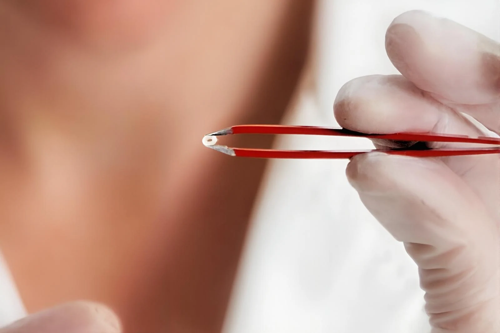 A gloved hand holding a micro-molded sample with tweezers