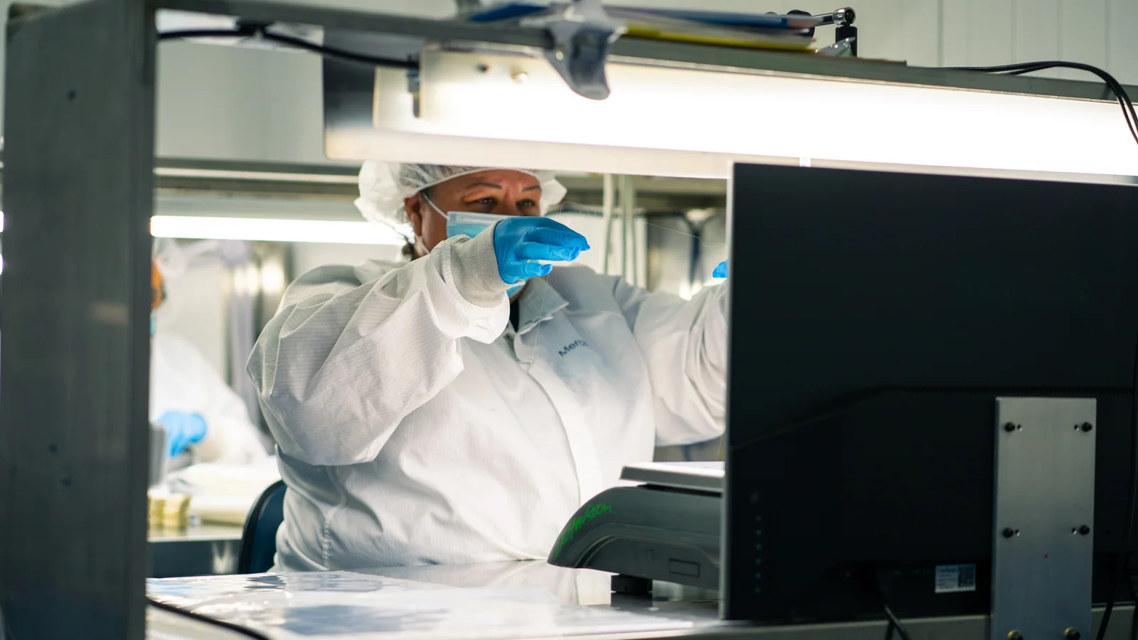 Cordica quality technician visually inspecting a medical component under task lighting